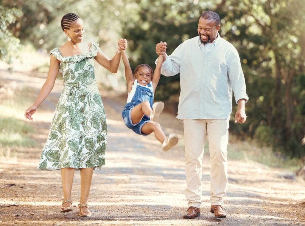 Happy parents swing girl at their hands in the forest during a walk in nature. Cheerful kid having