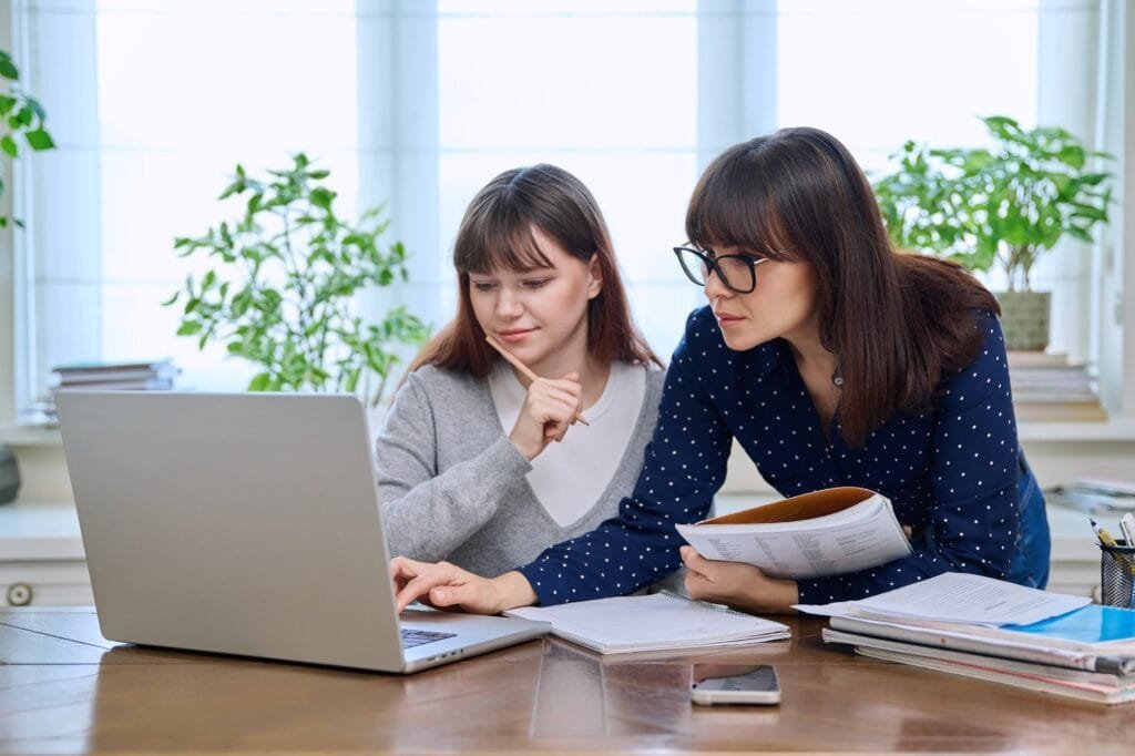 Teenage student studying at desk with computer, trainer mentor helping teaching